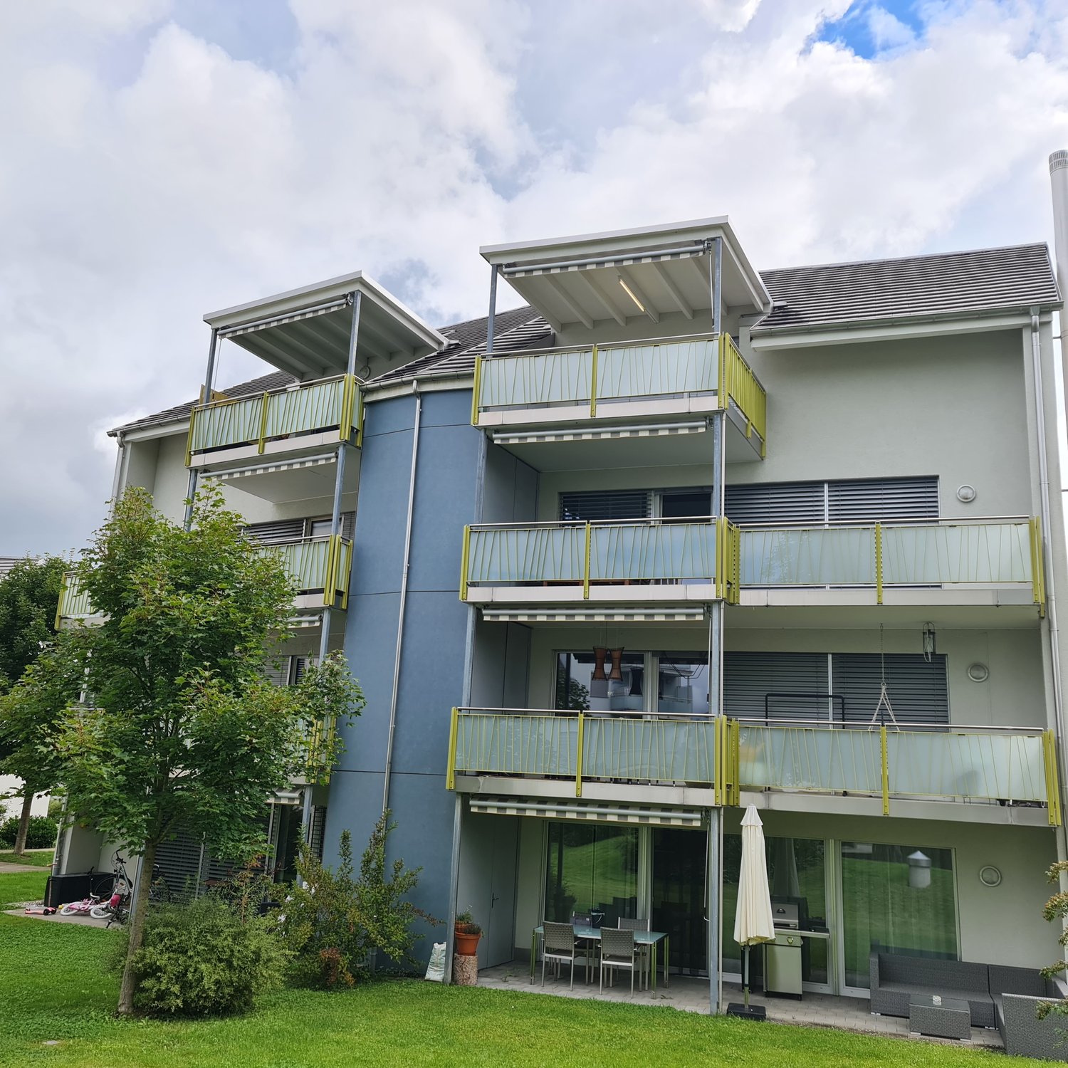 Apartment building, 4 stories, blue and white, multiple balconies, glass doors and windows, green lawn in front