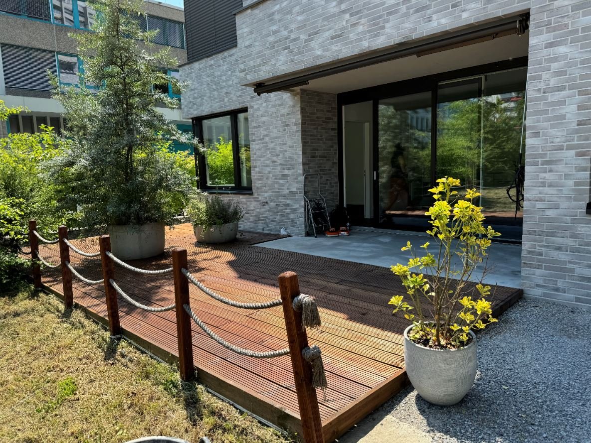 wooden decking with rope railing, 3 large potted plants, paved area