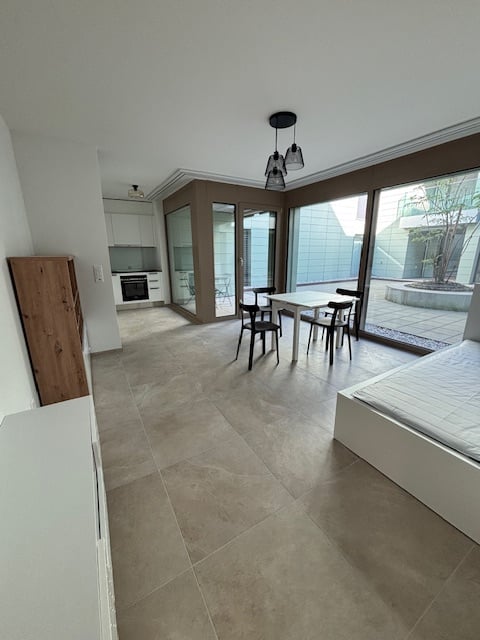 modern interior, white walls, tiled floor, white bed, white table and chairs, wooden cabinet, kitchen area with oven