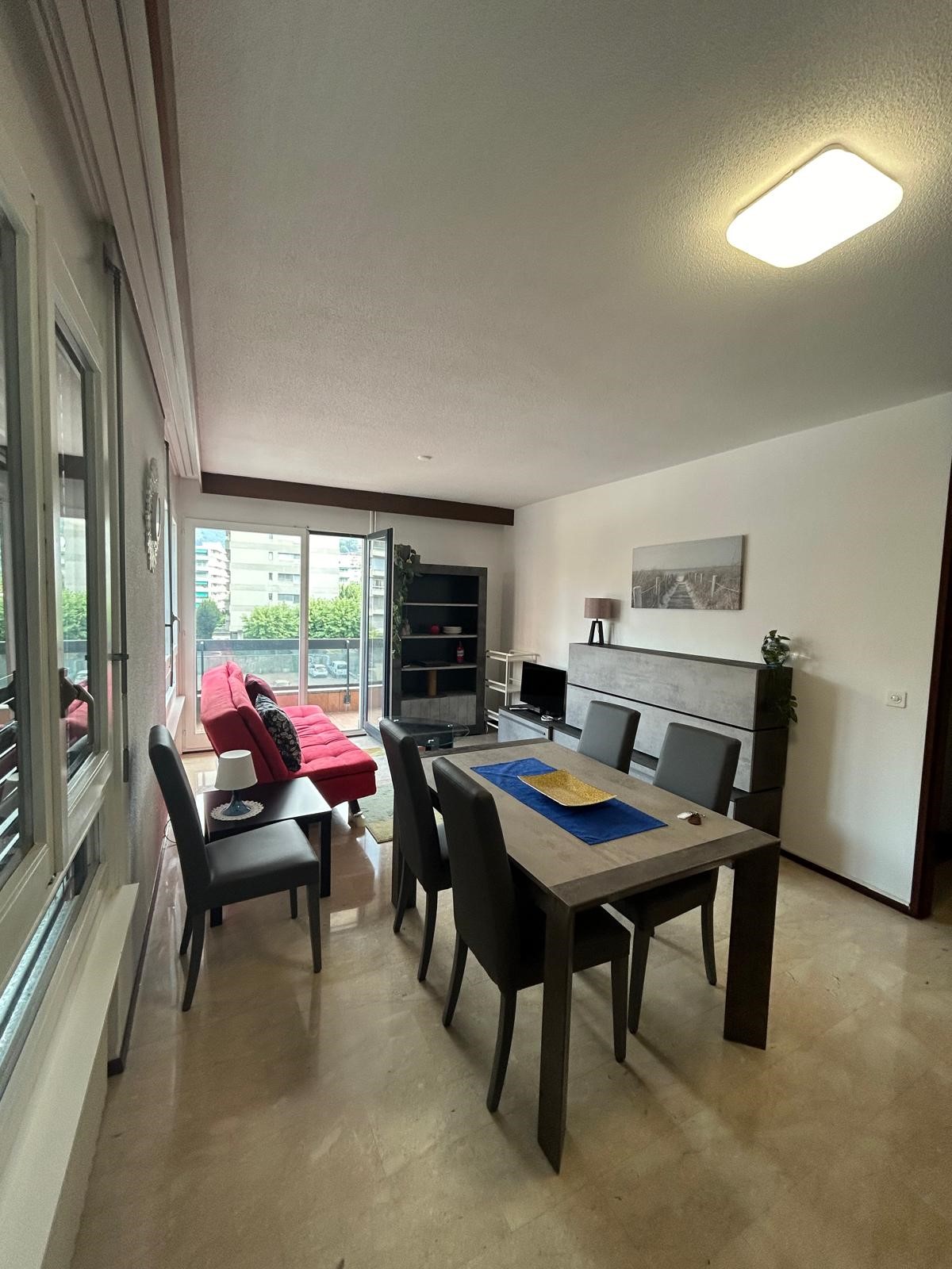 open space living room with large windows, balcony access, dining table, sofa, TV stand, floor lamp
