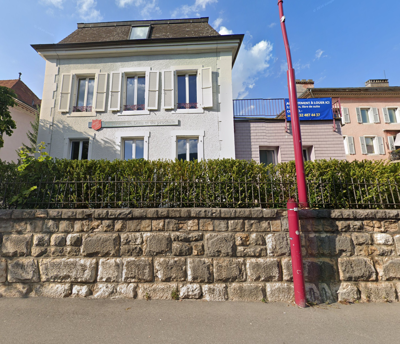 White house, red roof, white shutters, stone wall, greenery, parking pole