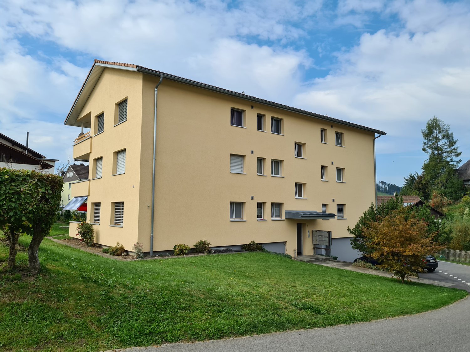 multi-unit residential building, yellow, multiple windows, balcony, garage, grass, tree