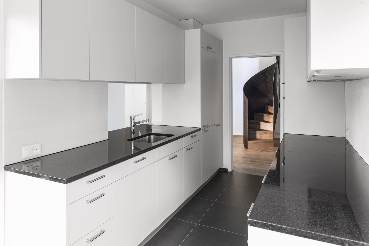 kitchen with granite countertops, white cabinetry, stainless steel sink, modern faucet, electrical outlet, open door with wooden staircase
