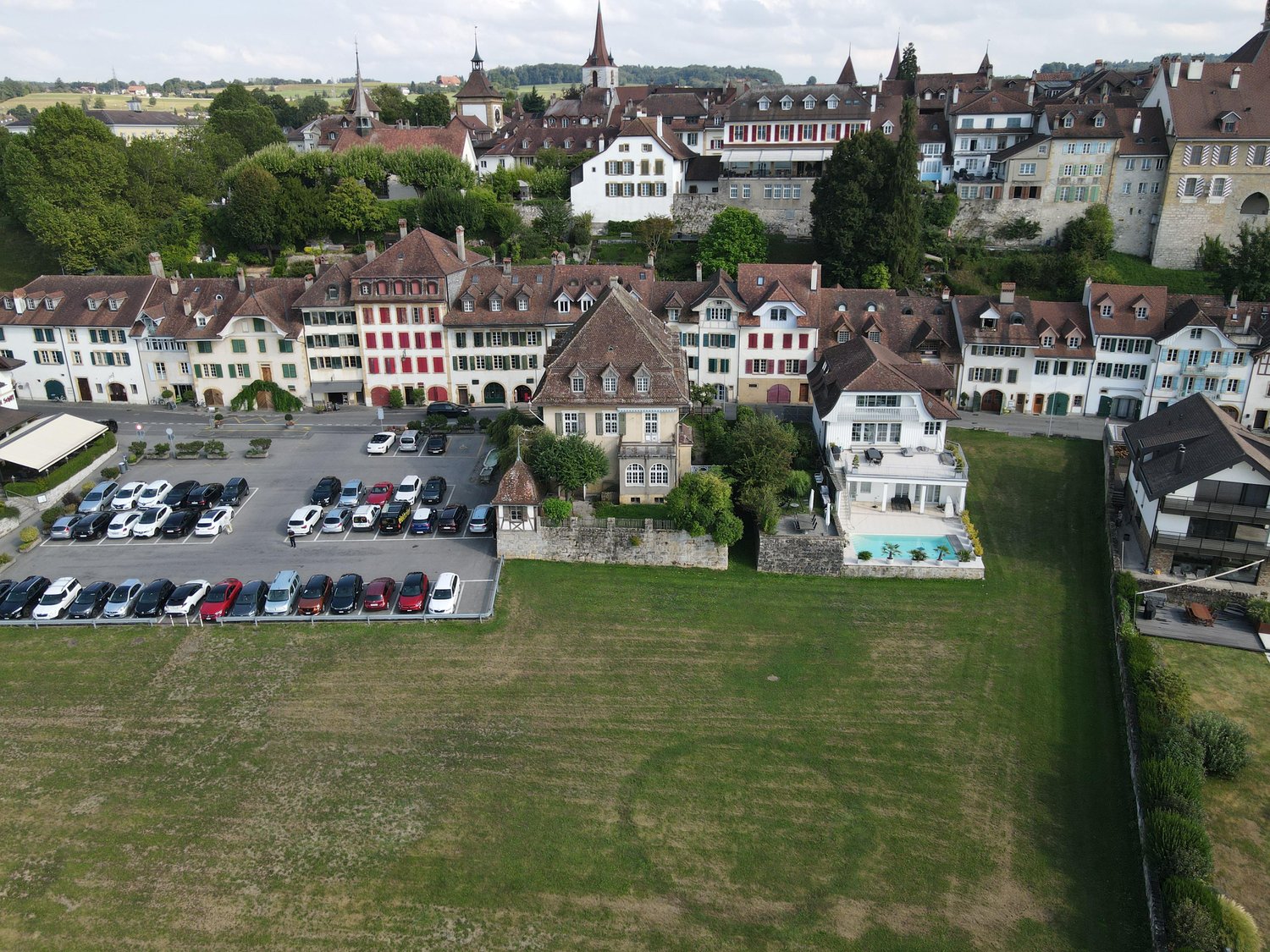 Many buildings, large parking lot, swimming pool, multiple vehicles