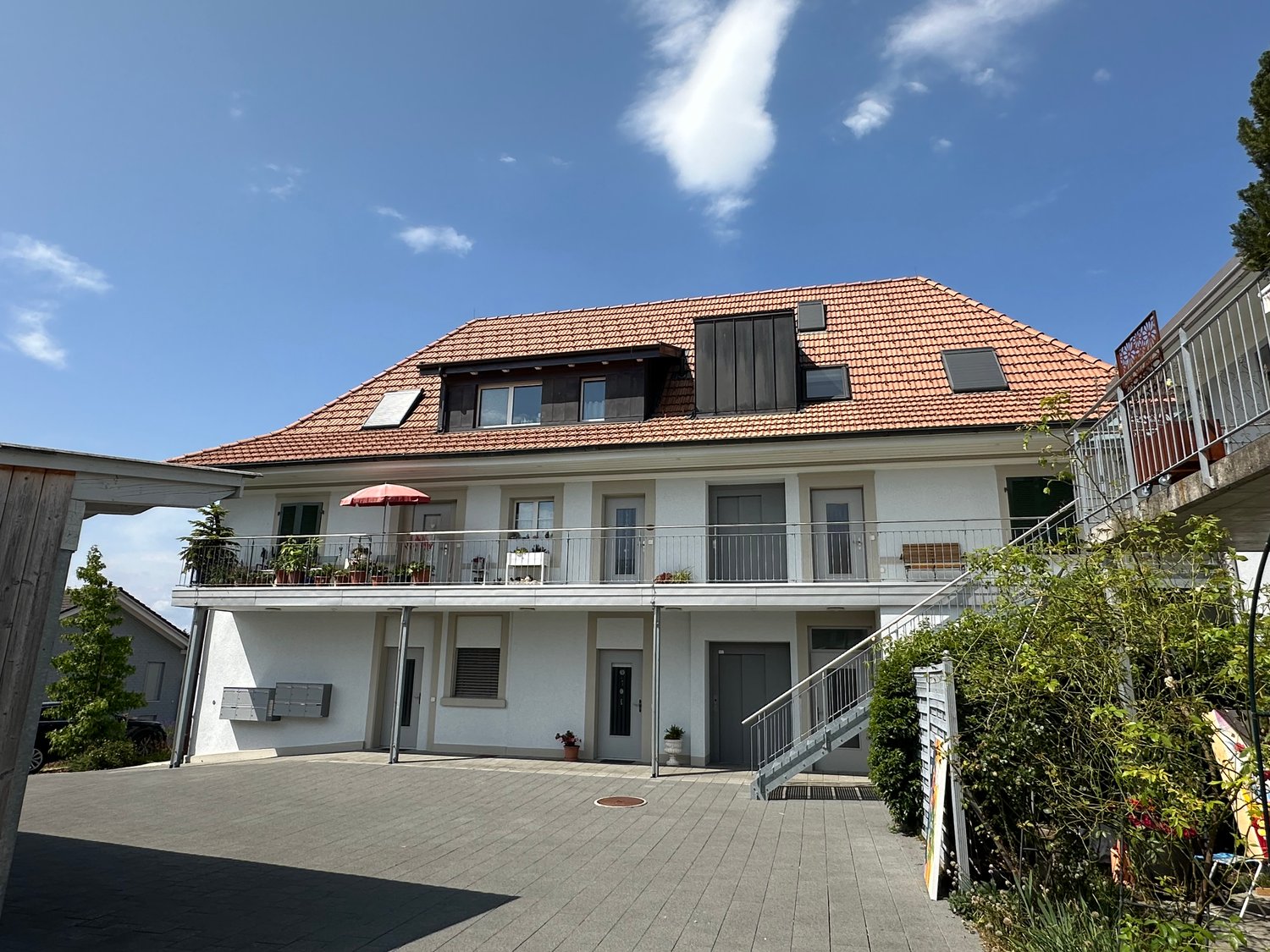Two story house, white walls, red roof, balcony, metal railings, plants, staircase