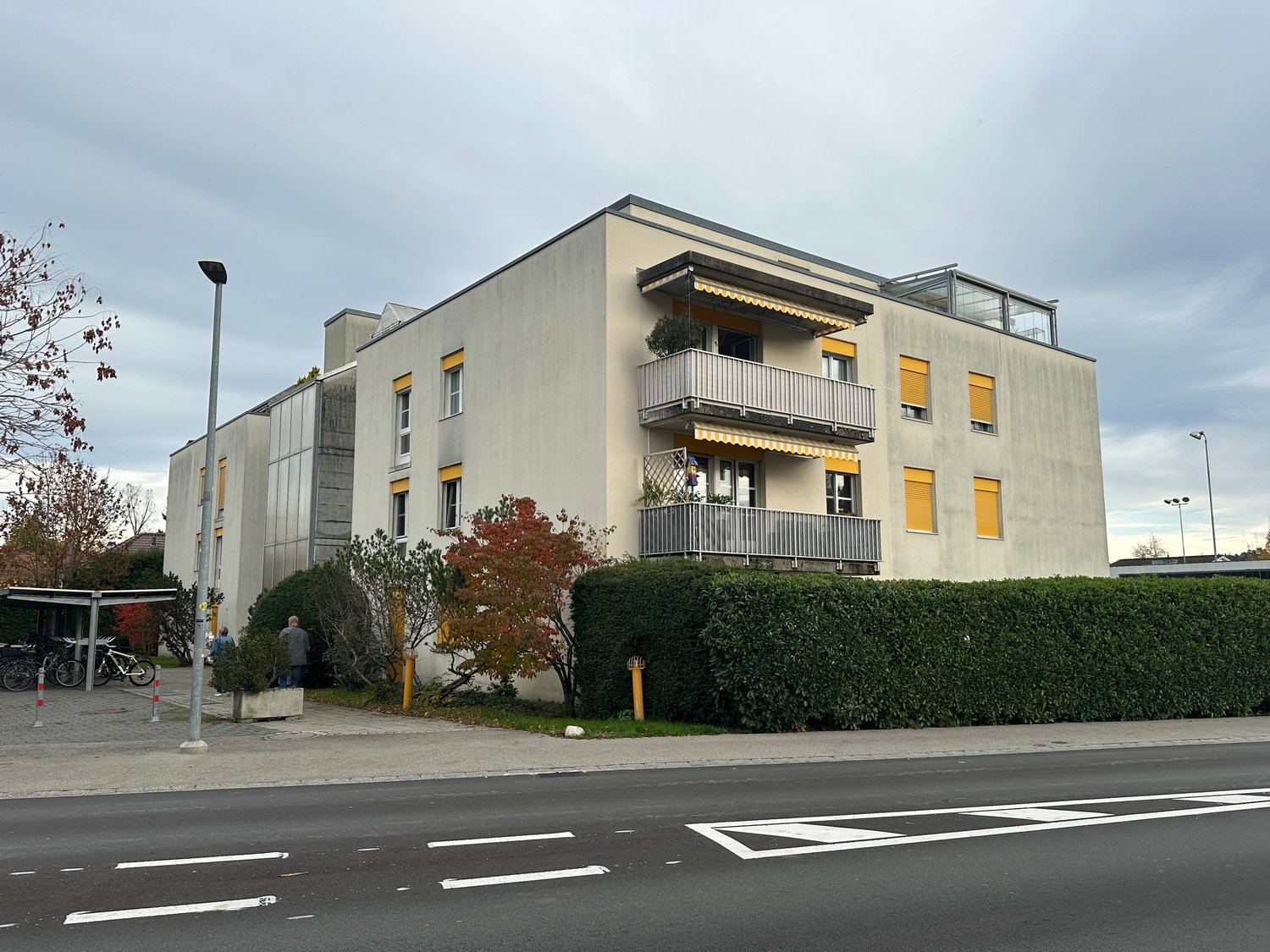three-story residential building, yellow windows, balconies, gray facade, street view