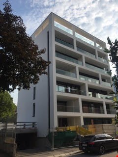Multi-story apartment building with balconies, glass windows, and a modern, minimalist design.