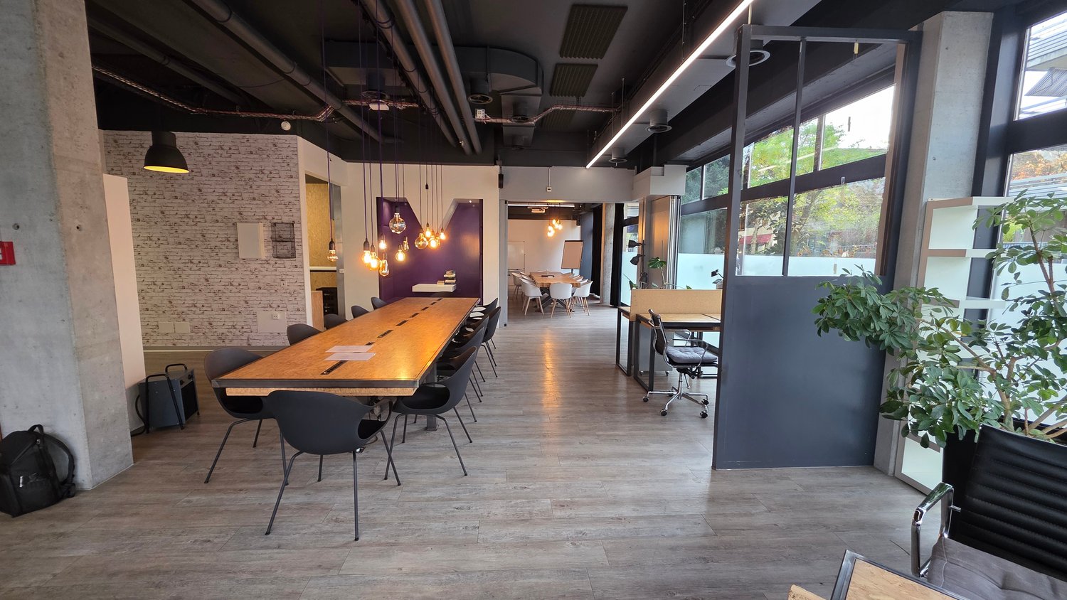 large open space with wood flooring, long wooden table, modern chairs, brick wall, bright windows, office setting