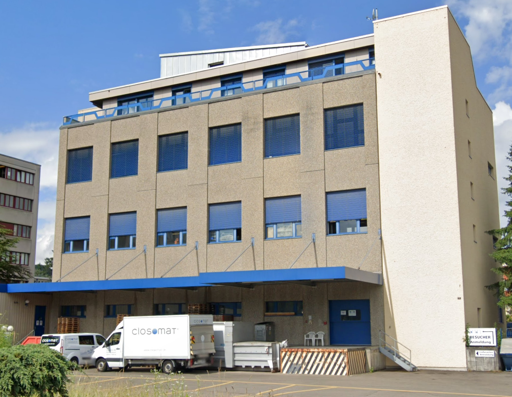 4-story building, blue shutters, blue canopy, white and brown exterior, several windows, blue doors, delivery trucks parked