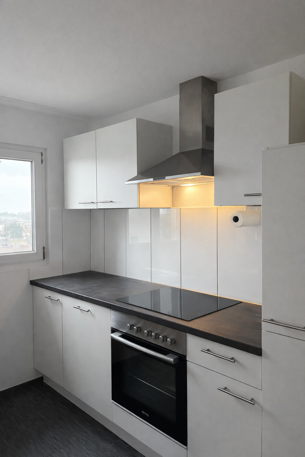 modern kitchen with white cabinets, black countertops, integrated stove and oven, stainless steel extractor hood, window with view