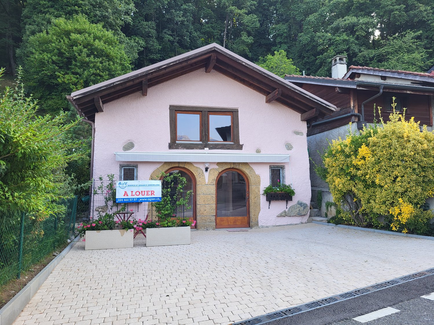 Two story pink house, wooden roof, arched windows, sign for 'A louer' (for rent), paved driveway