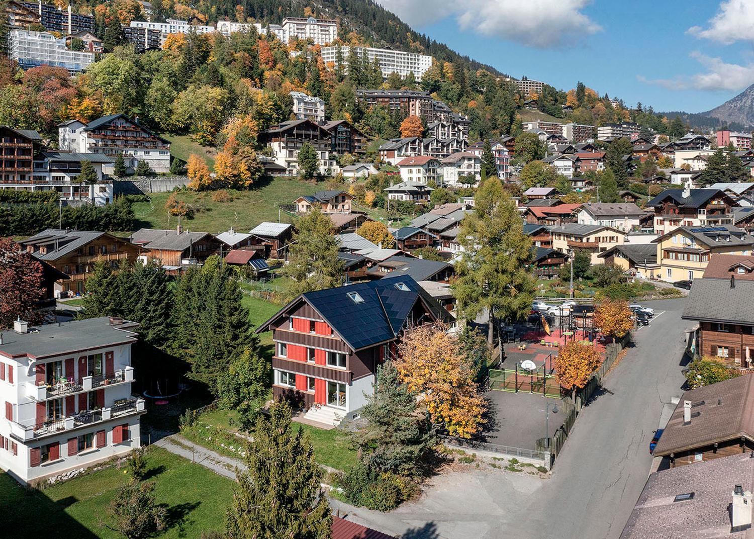 Swiss Alpine houses on a slope, surrounded by trees, small solar panels on the roof of the house in the foreground