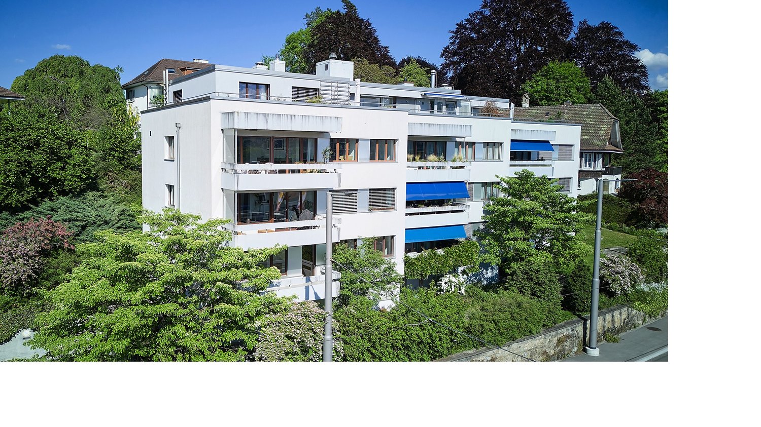 3 story building, modern architecture, white exterior, blue awnings, multiple balconies, greenery