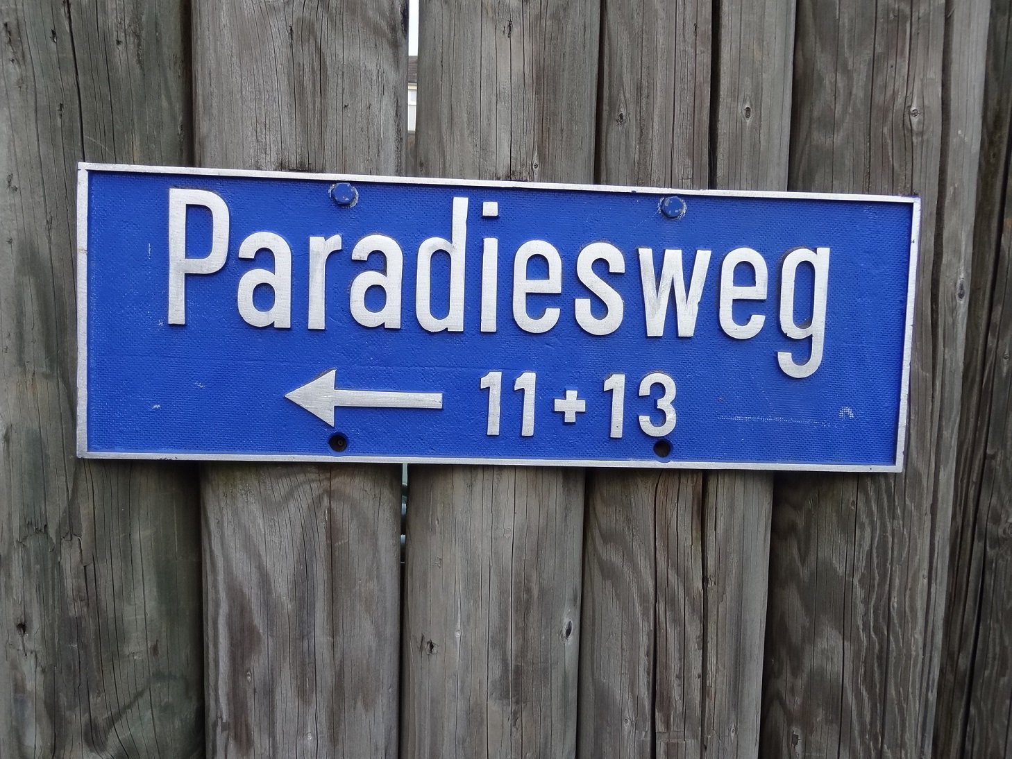 Blue sign with white text reading 'Paradiesweg 11+13' and an arrow pointing to the right