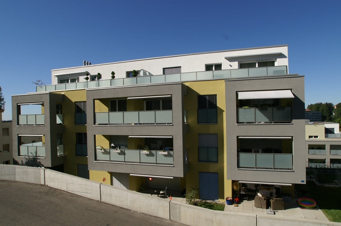4-story building, yellow and white, multiple balconies with awnings, concrete fence around the ground floor