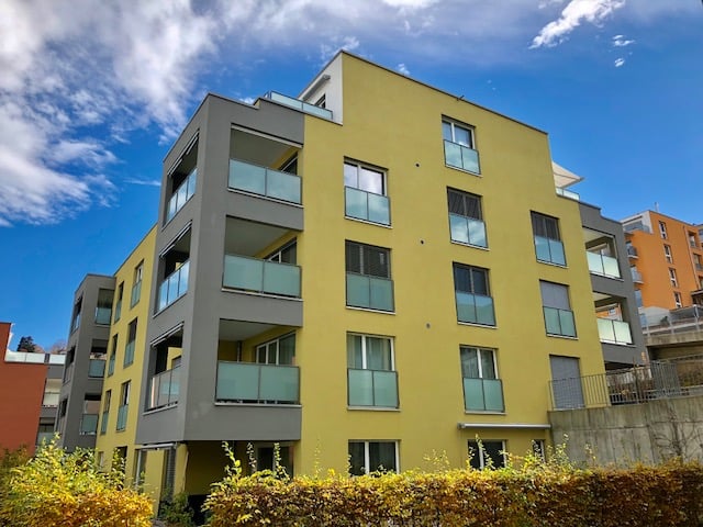 yellow building, gray accents, many glass windows, balconies, hedges