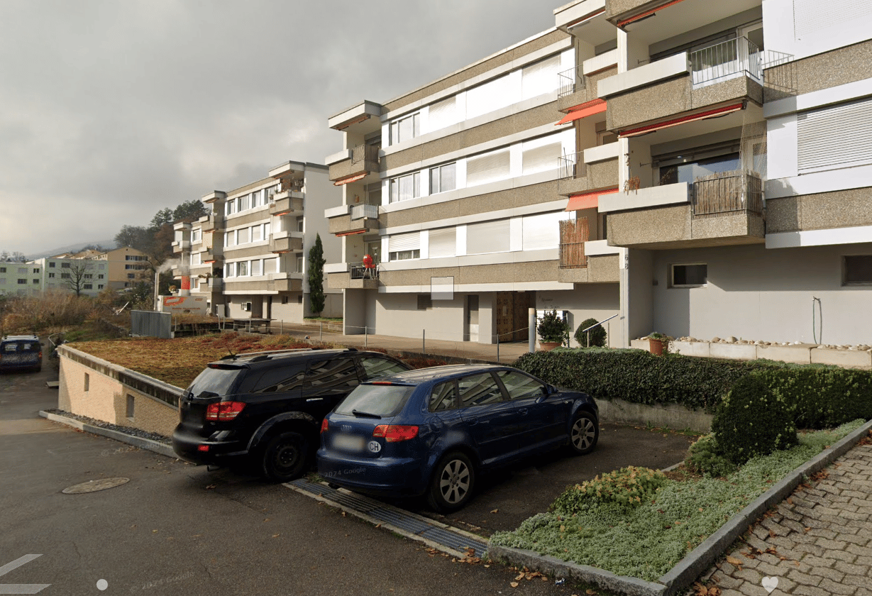 Apartment building with multiple floors, balconies, and parking spaces in front.