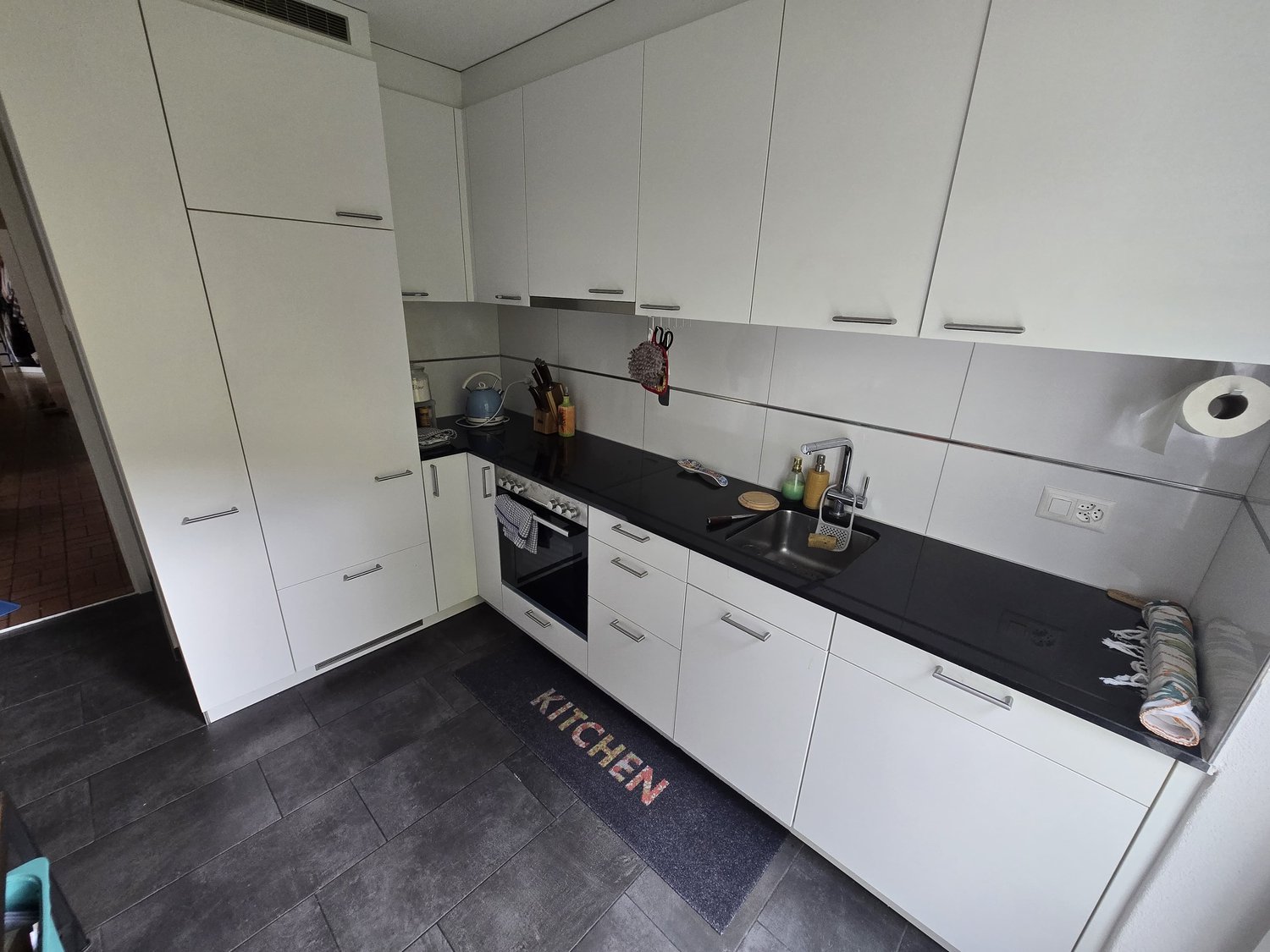 modern kitchen with white cabinets, black countertop, sink, oven, dishwasher, washing machine, countertop rug, and various kitchen tools and appliances