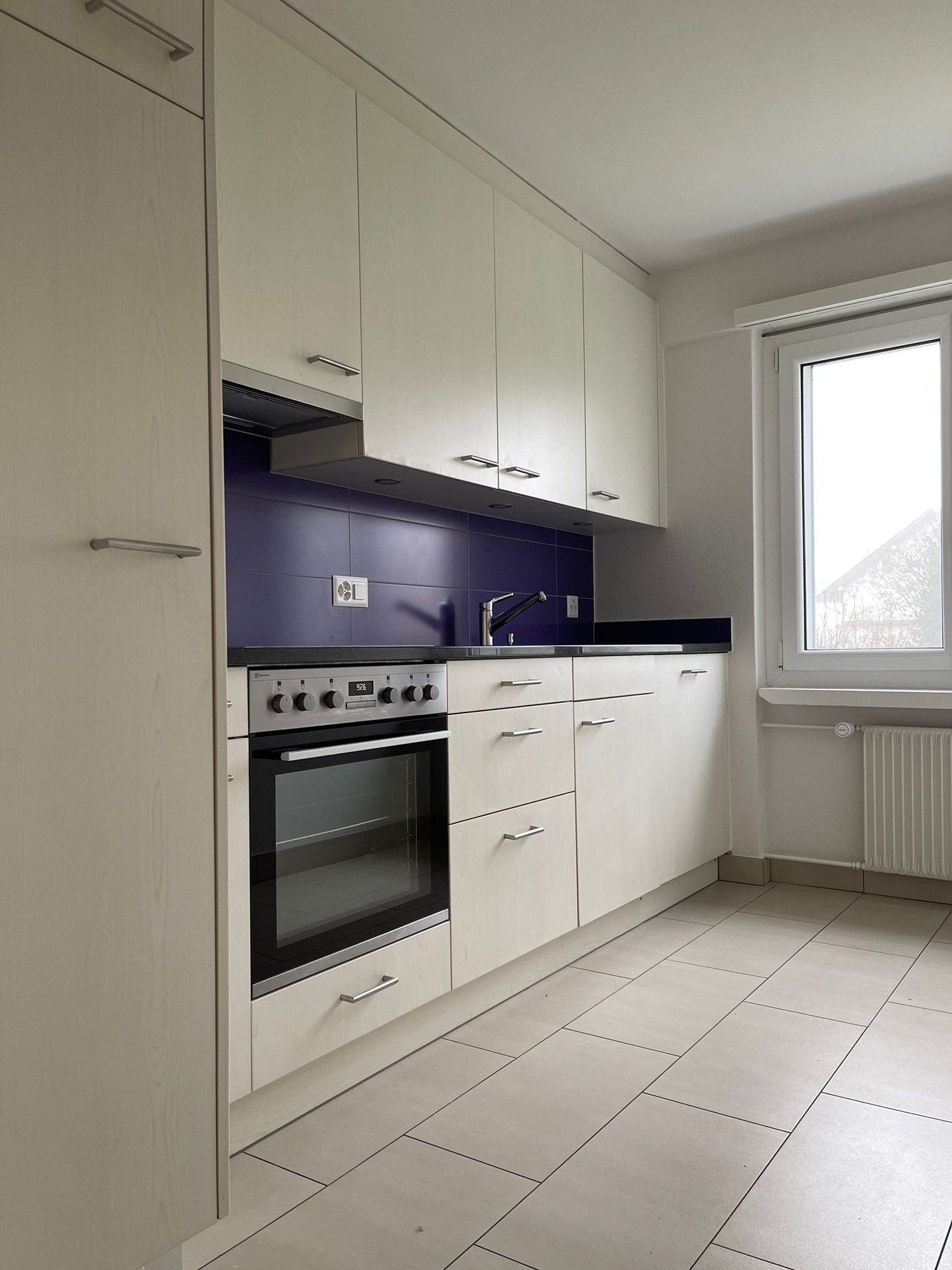 kitchen with white cabinets, blue backsplash, electric stove, oven, sink with faucet, tile flooring