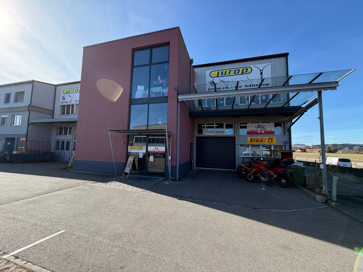 Commercial building with glass facade, roll-up doors, outdoor awning, parking area, motorcycle parked in front