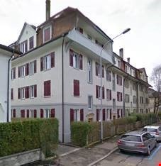 5 story building, white walls, red shutters, cars parked on the street