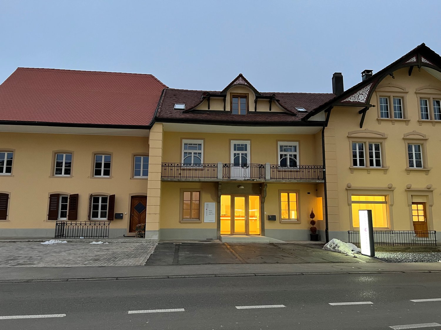 2 story yellow house, red roof, wooden doors, wooden shutters, balcony with railings, large windows, side entrance