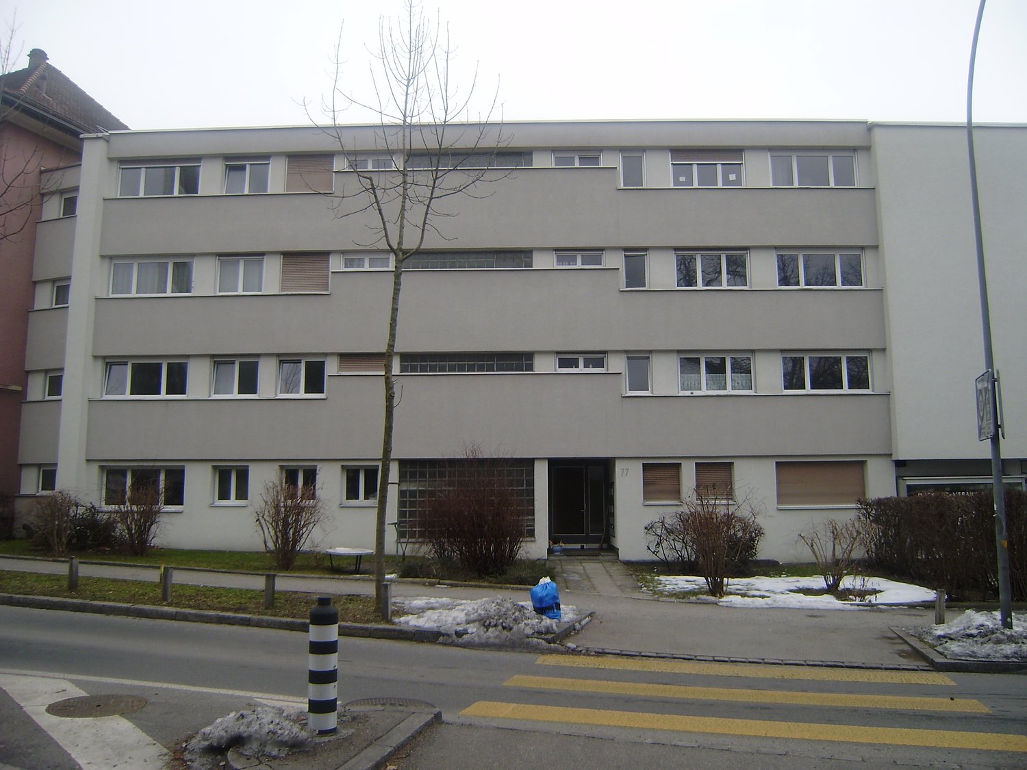 4 story apartment building, white exterior, multiple windows, entrance with a door, tree in front
