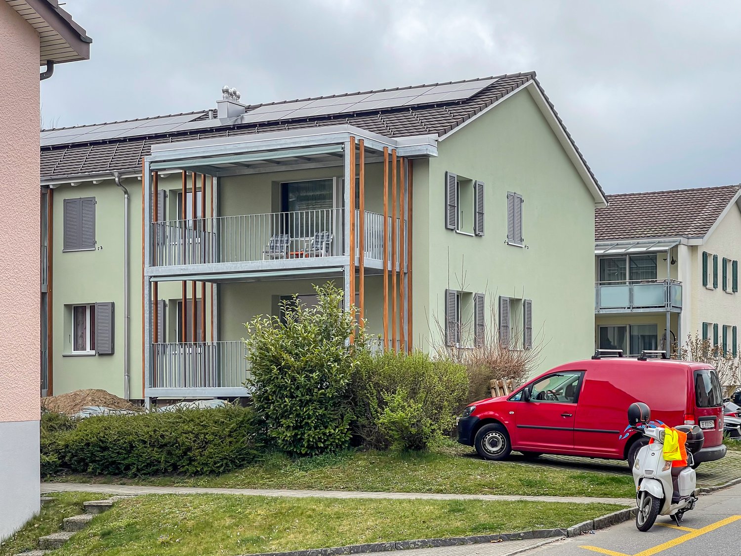 2-story apartment building, green paint, solar panels, balconies, street, parked van, parked scooter