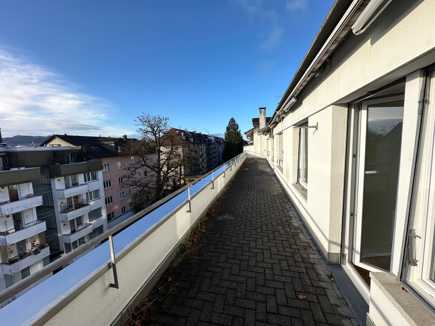 View of a roof terrace with paved floor, metal railings, and a clear view of the skyline.
