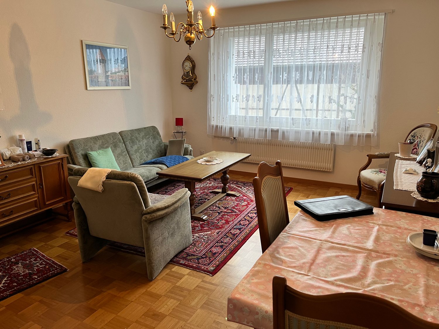 living room with couch, wooden table, radiator, chandelier, window, rug, dining table, wooden floor