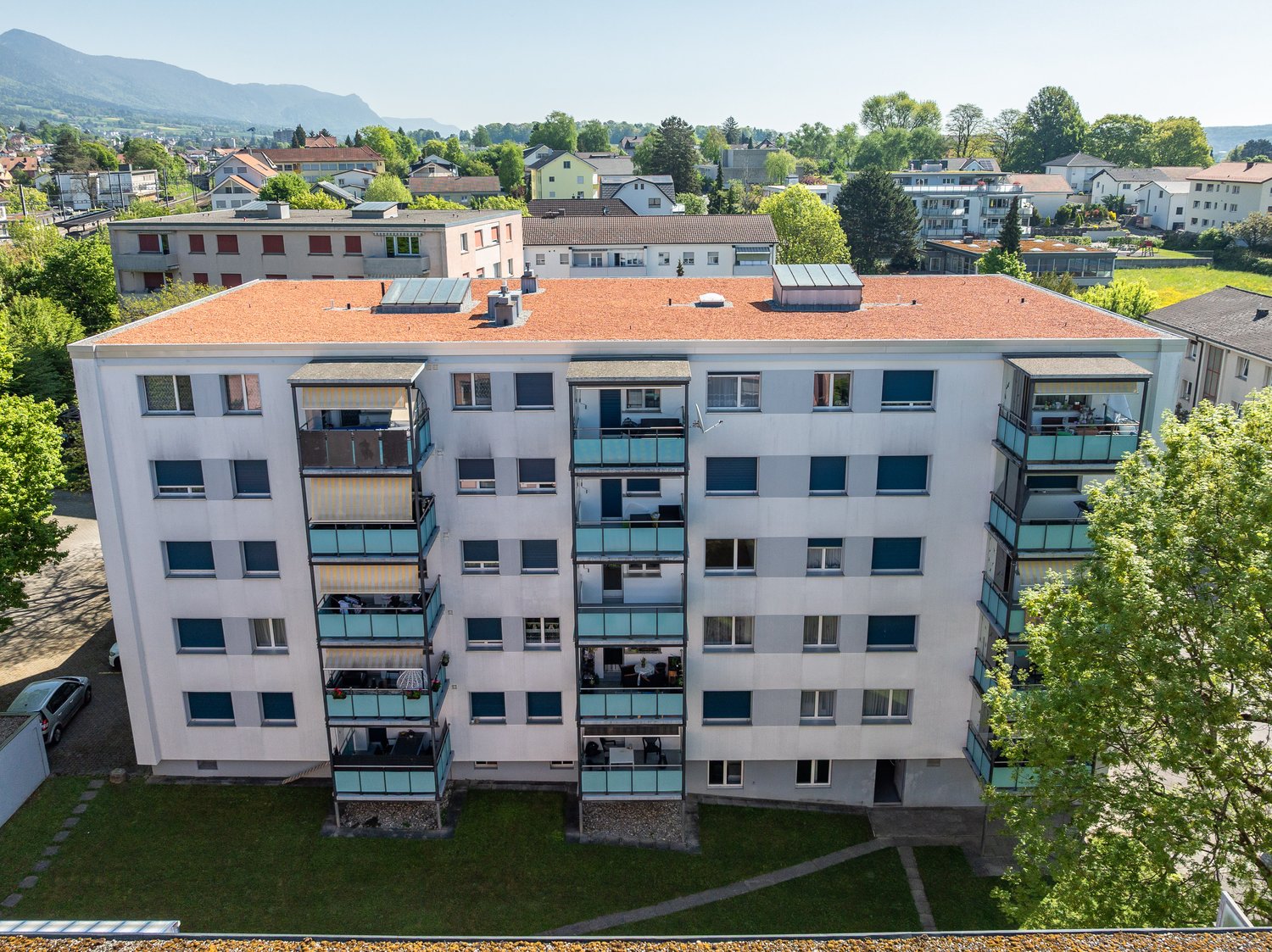 Multi-story apartment building, red roof, multiple balconies, windows, outdoor car park