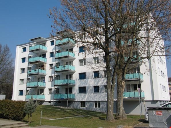 White building with multiple floors, several balconies, and a grassy lawn.