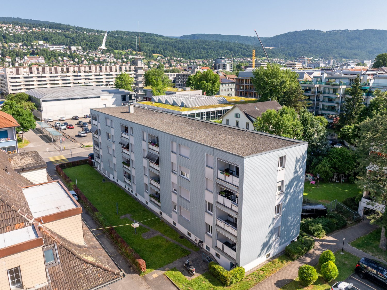 Multi-story residential building, balconies on each floor, green grass on the ground floor, trees and plants around the building