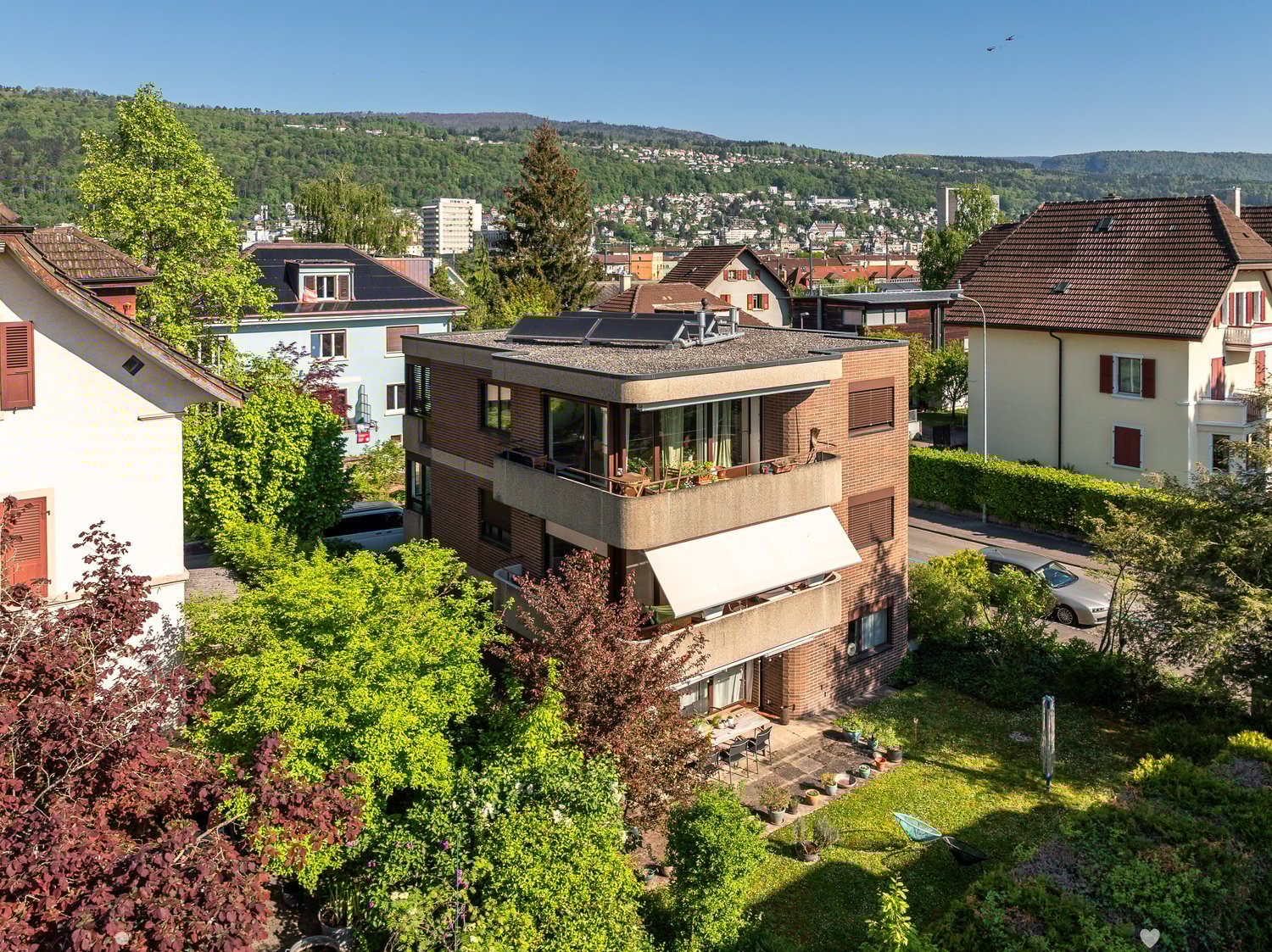 multi-story residential building, solar panels on the roof, balcony on the front side, garden, distant mountain view