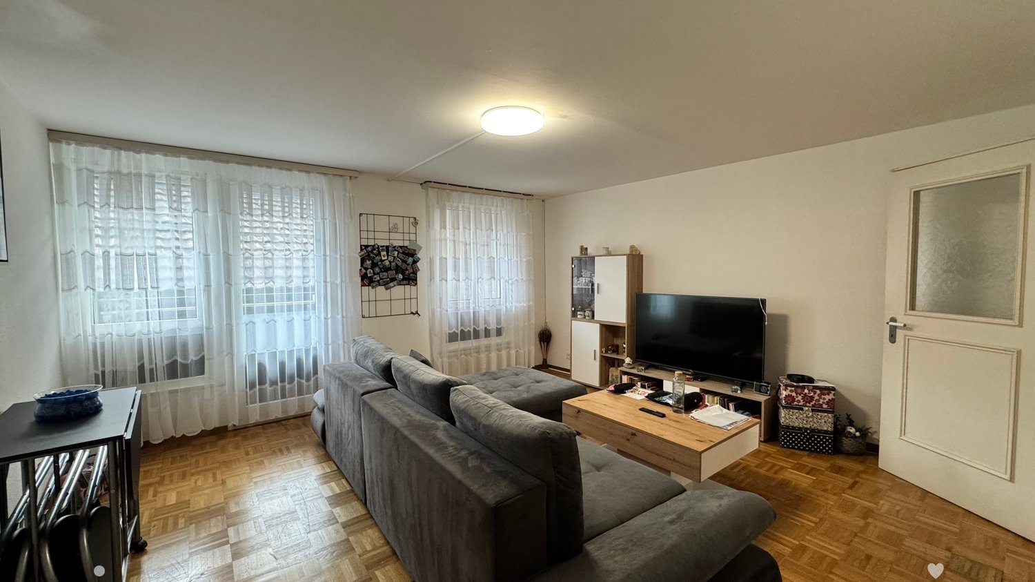 grey sofa, coffee table, television, shelves, windows with white curtains, hardwood flooring