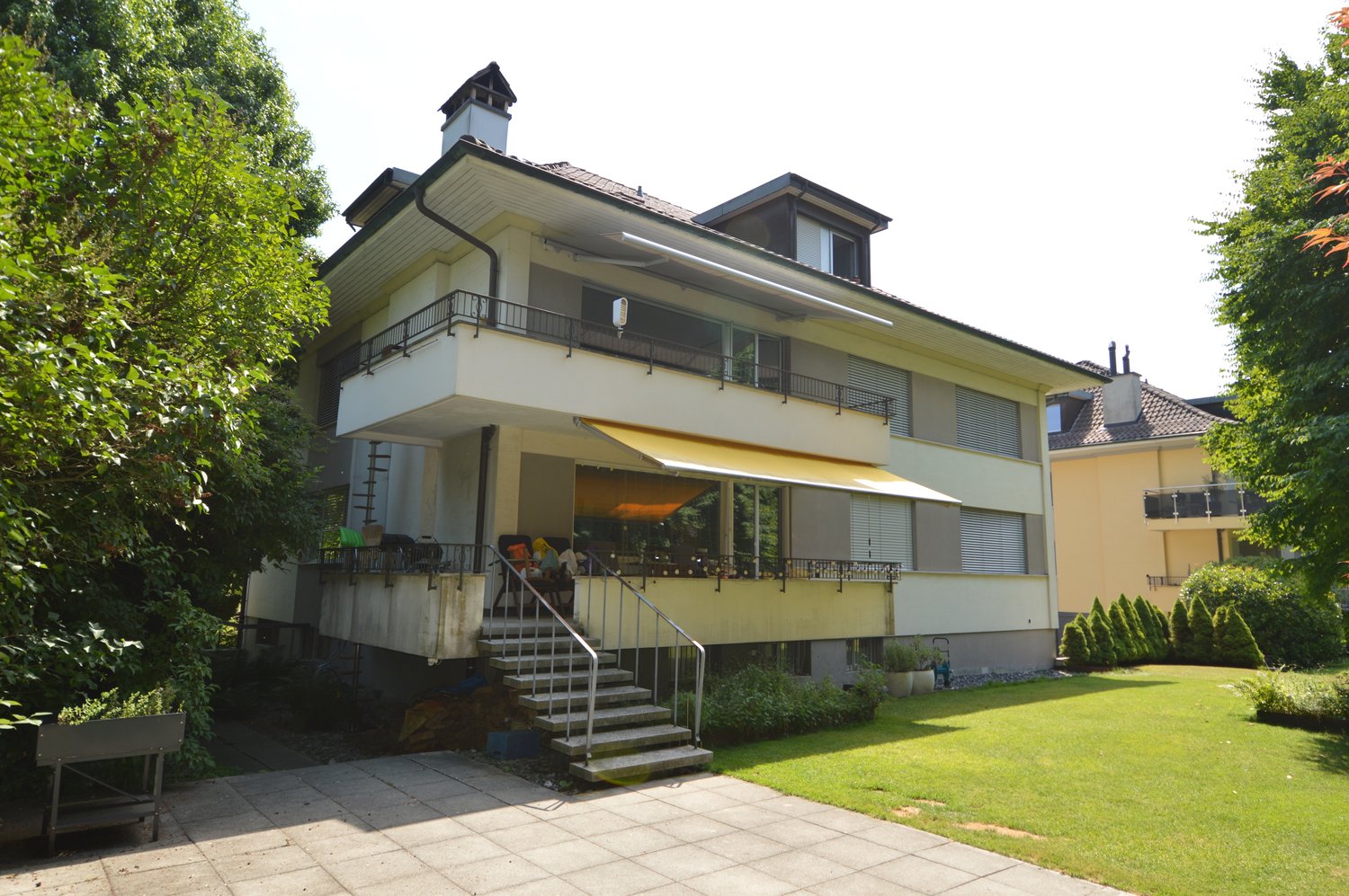 2 story house, beige exterior, brown roof, balcony, stairs, garden, lawn, chimney, multiple windows