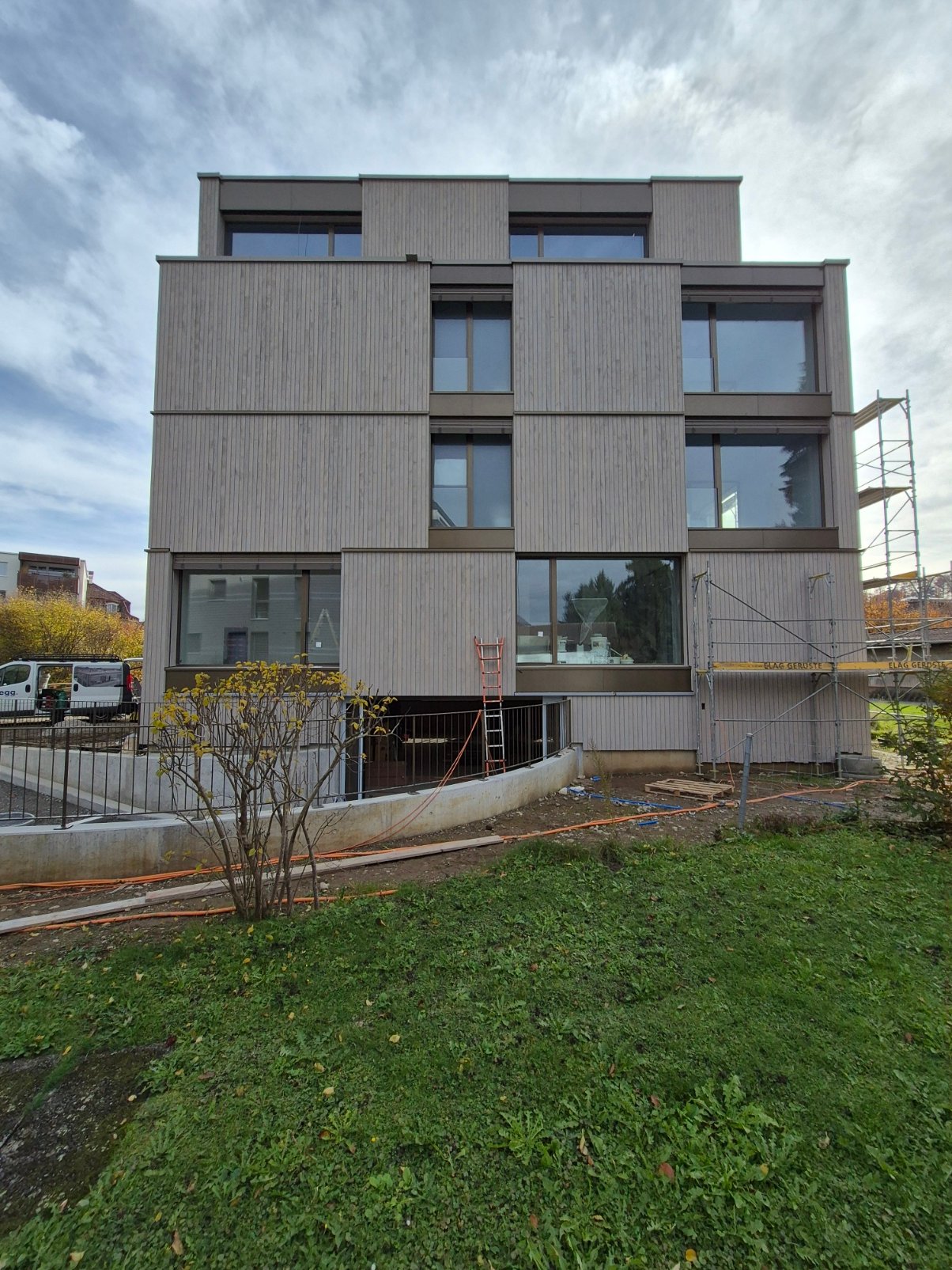 Modern 4 story building with multiple windows, under construction, wooden panels, scaffold on side