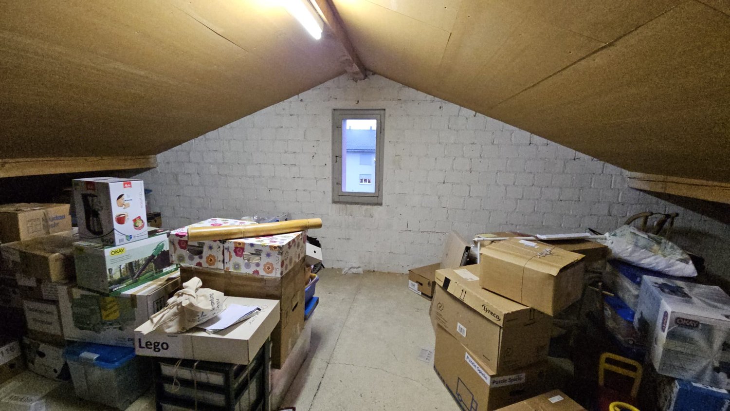attic with boxes and furniture, sloped ceiling, white walls, small window, dim lighting