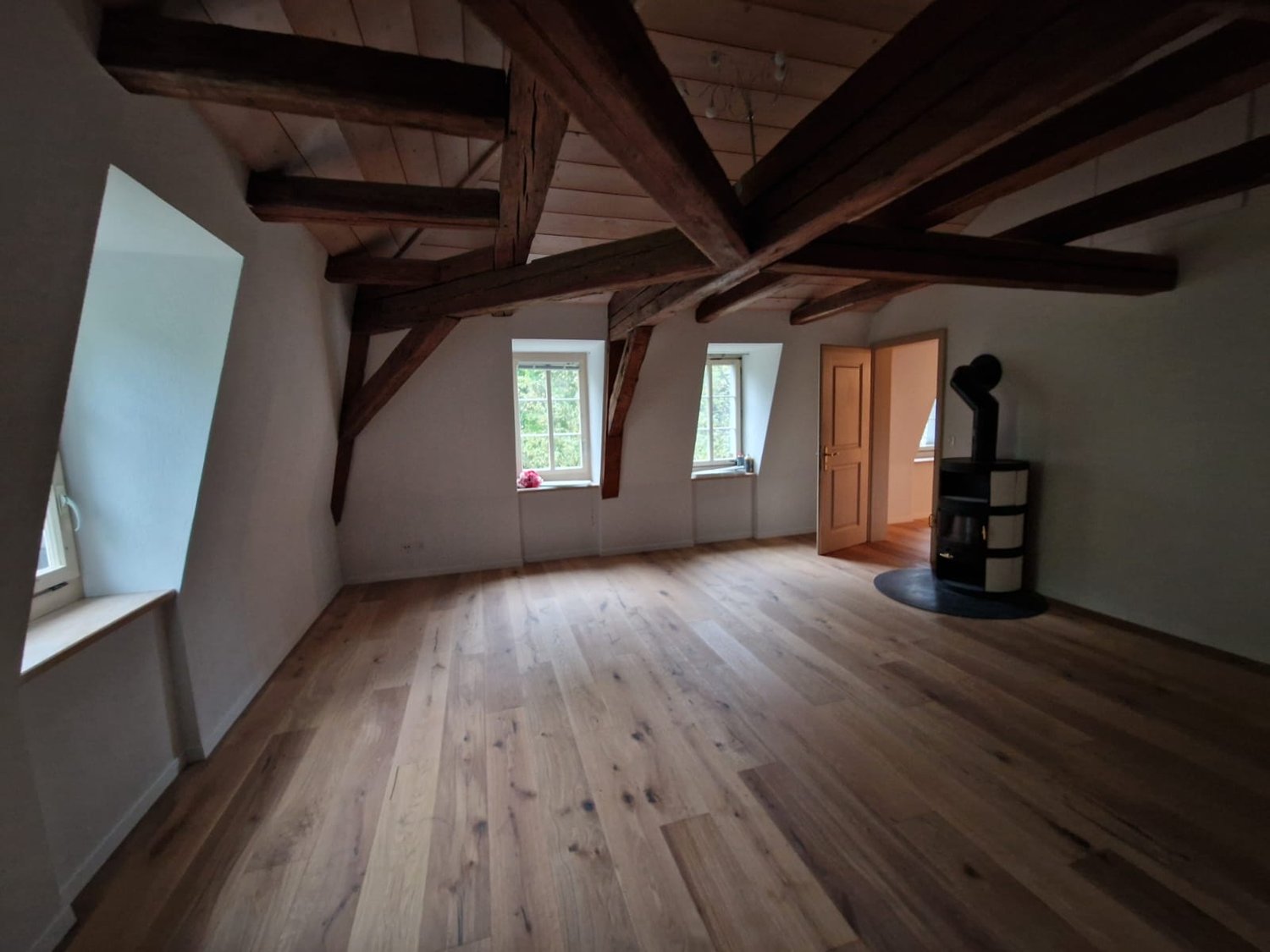 wooden floor, exposed wooden beams, two windows, wooden door, fireplace