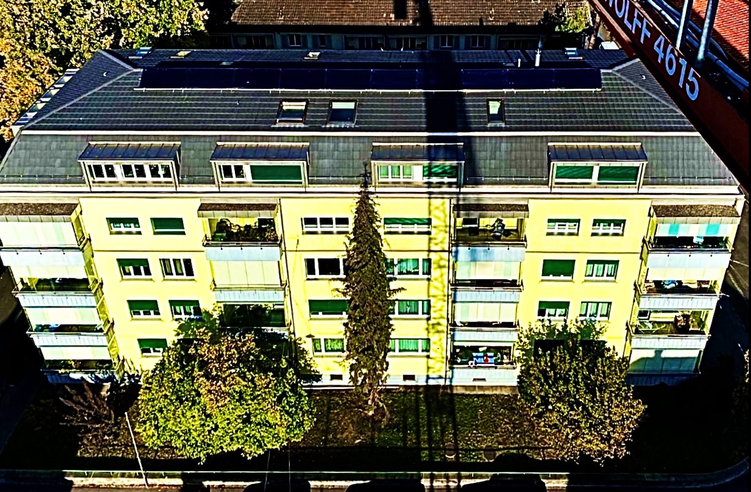 A yellow apartment building with multiple balconies on each floor, multiple windows, solar panels on the roof