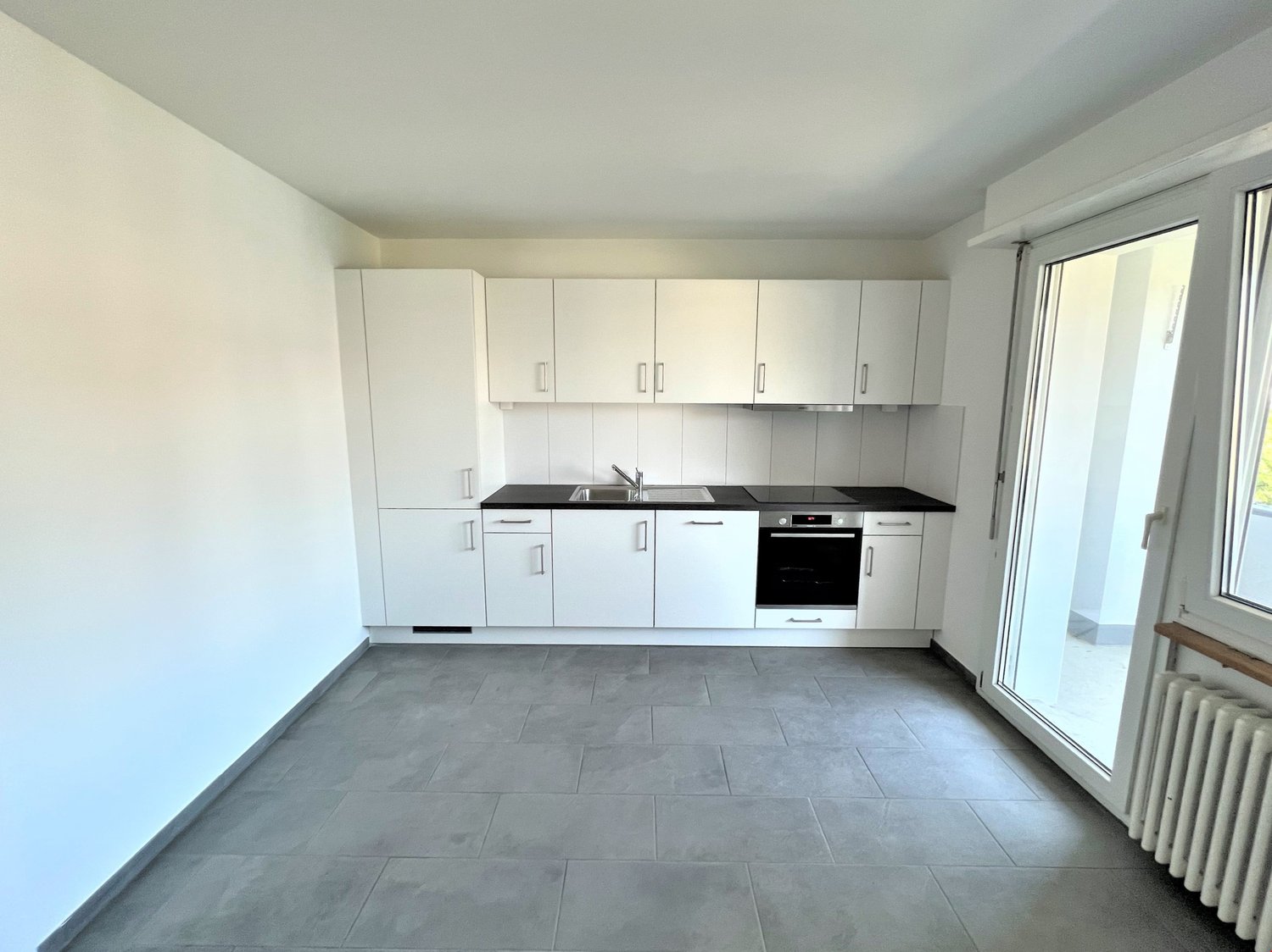 white cupboards, black countertops, integrated dishwasher, built-in oven, sink, sliding door, large glass door, radiator