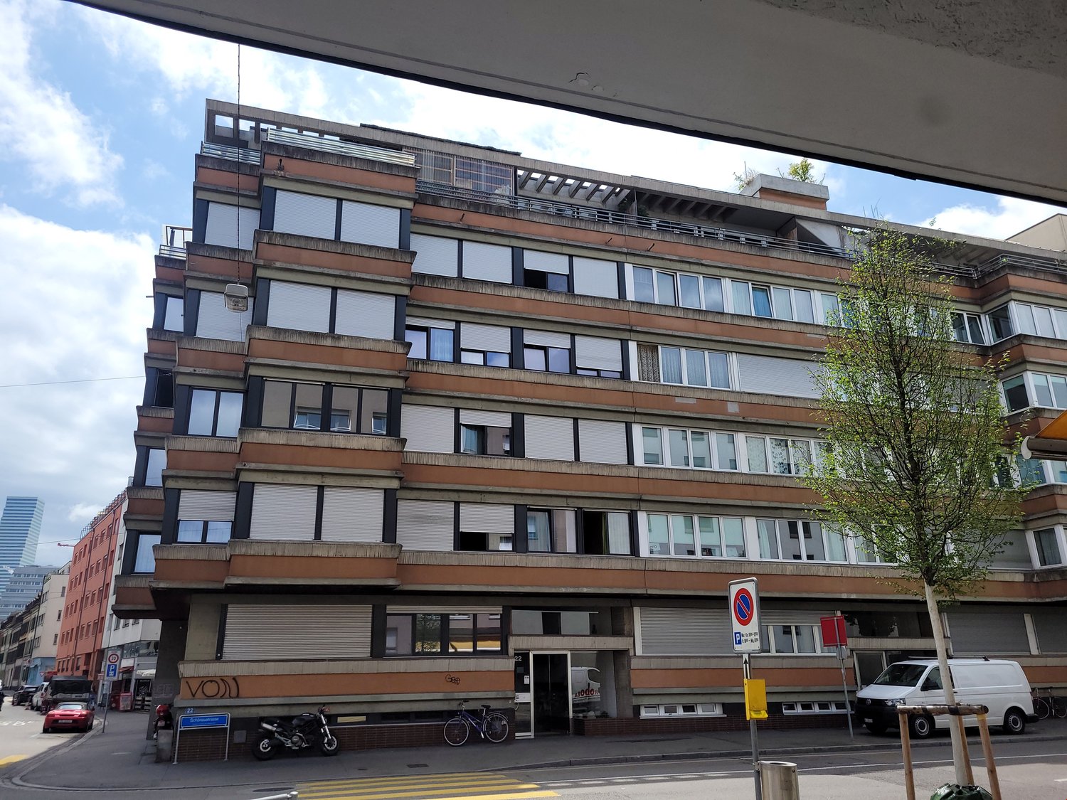 Multiple floor building, with balcony on multiple floors, large windows, brown and white walls, bicycles parked outside