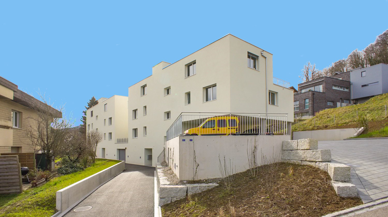 white modern building, raised ground floor with yellow car, paved road, paved parking area in front