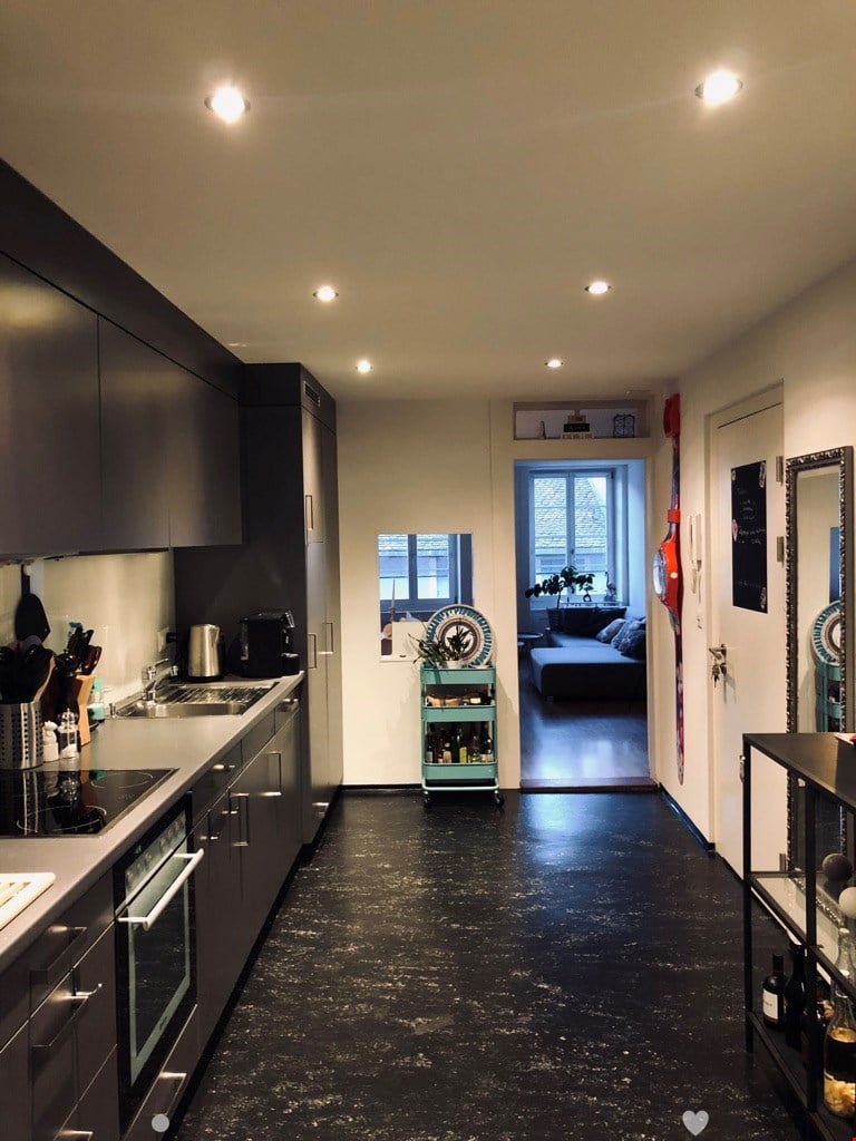 Black and white kitchen with a sink, faucet, oven, modern cabinets, kitchen cart with plants, and various kitchen utensils