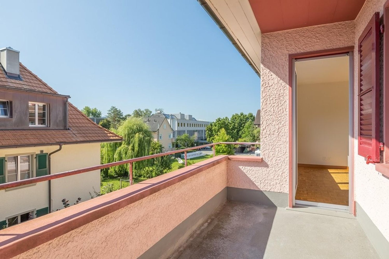balcony with wooden railings, tiled floor, green shrubs in the background