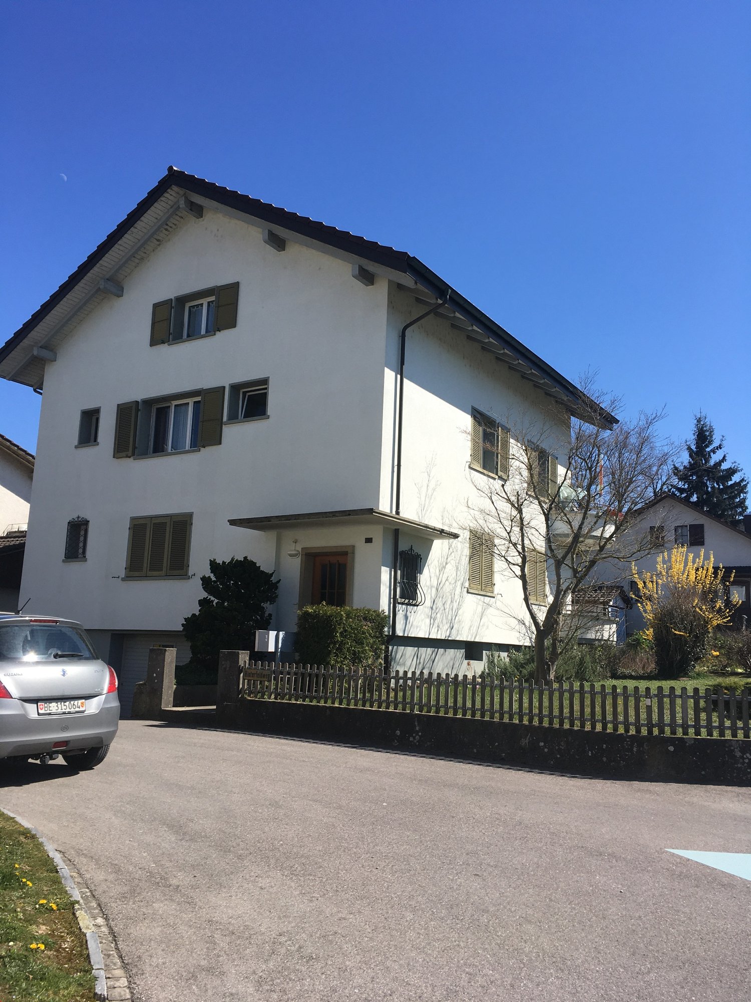 3 story house, white exterior, brown roof, multiple windows, small garden, driveway