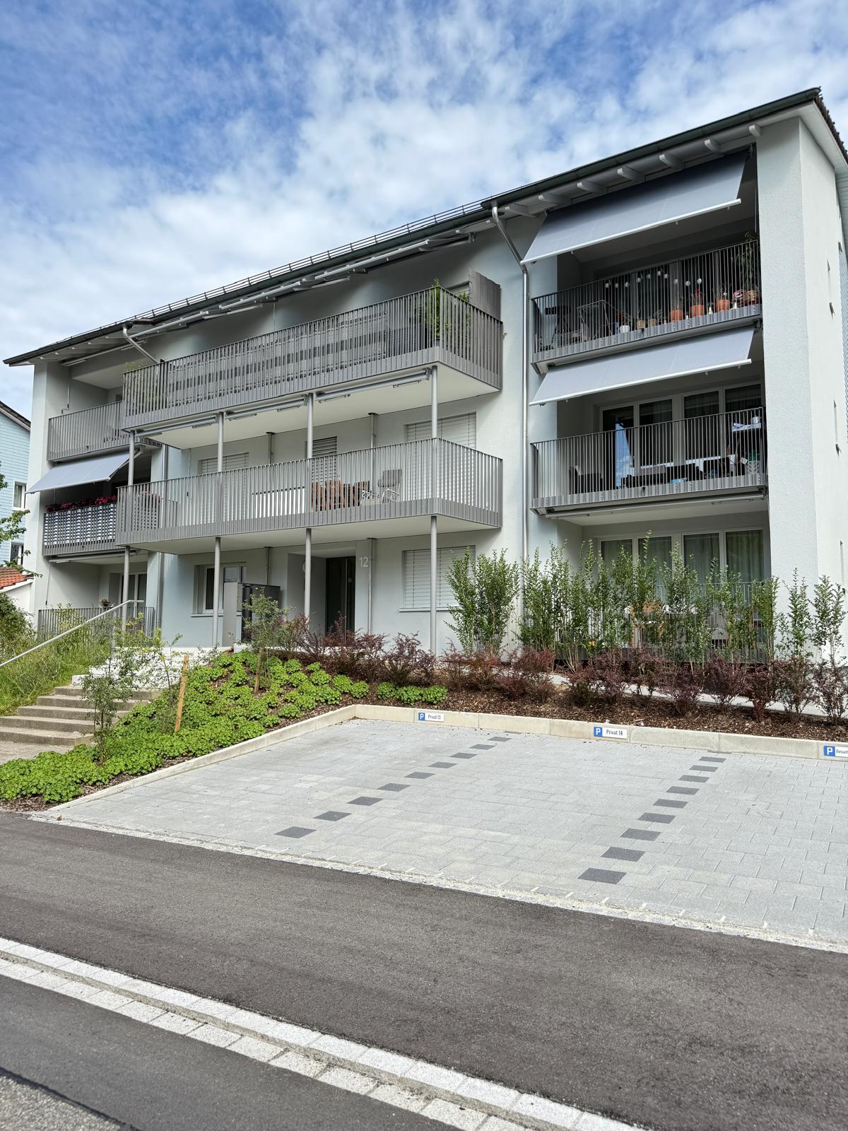 3 story building with balconies, paved parking lot, greenery in front