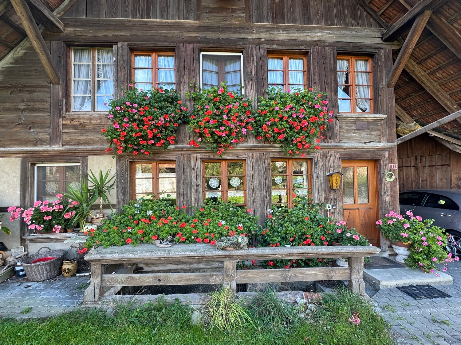 Old wooden house, exterior covered with flowers, wooden porch, small garden, car parked in front
