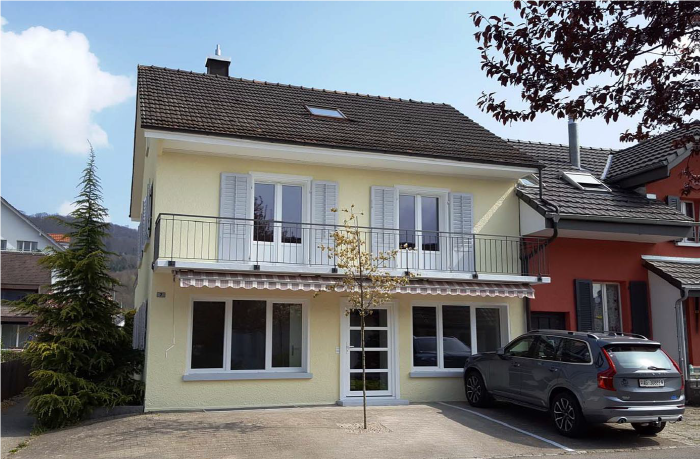 2-story house with yellow exterior, tiled roof, balconies, and a parked car in the driveway