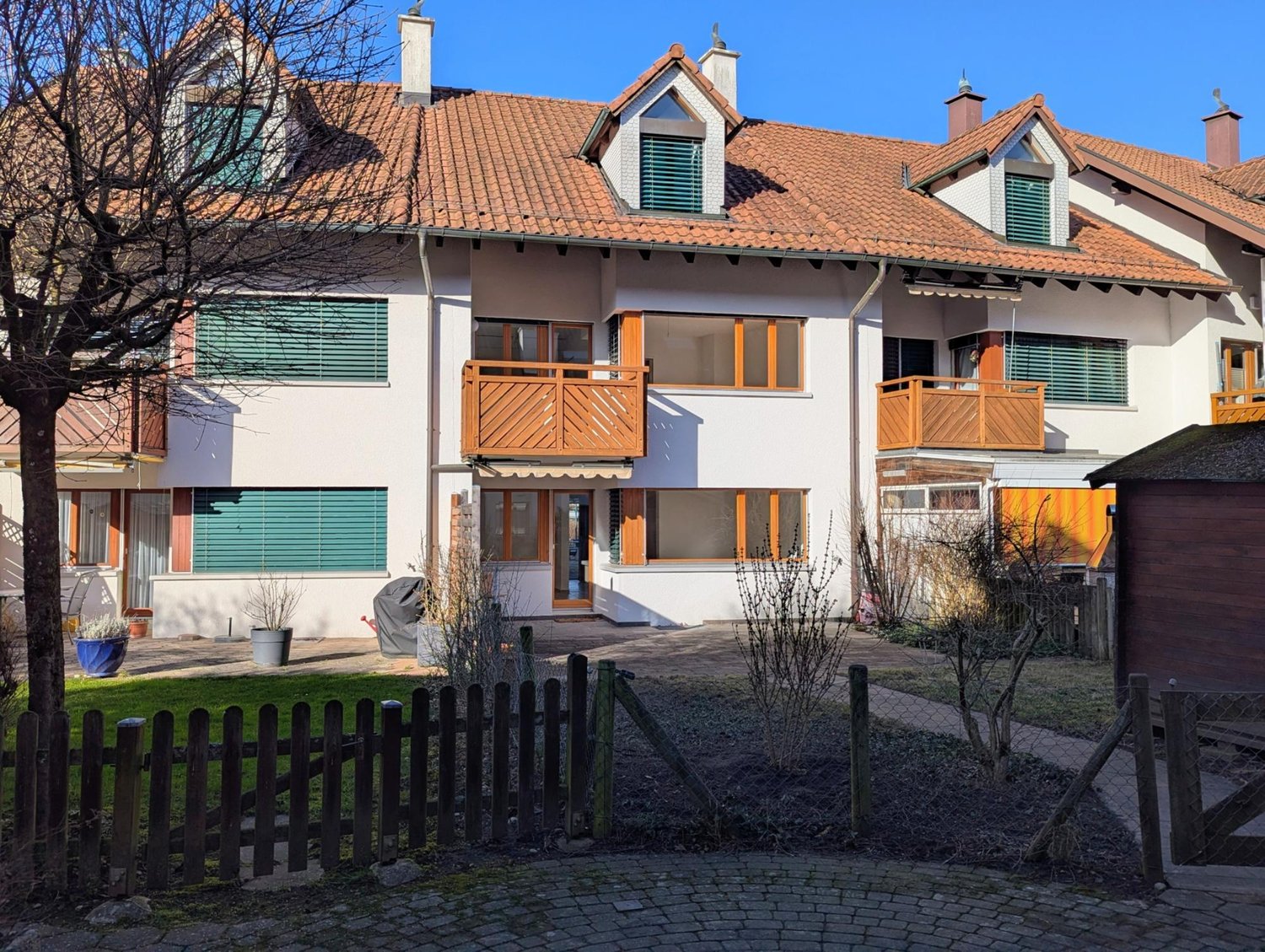 3 story apartment building, brown roof, white walls, wooden balconies, small garden, wooden fence